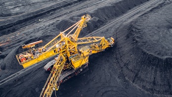 A photograph of a large coal mine and yellow heavy machinery