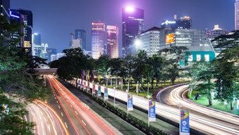 Photo depicts traffic, captured with blurred motion as light trails, rush along Sudirman street in Jakarta business district at night in Indonesia capital city.